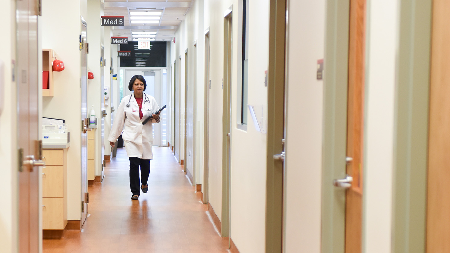 A doctor walks down a hallway of examination rooms at